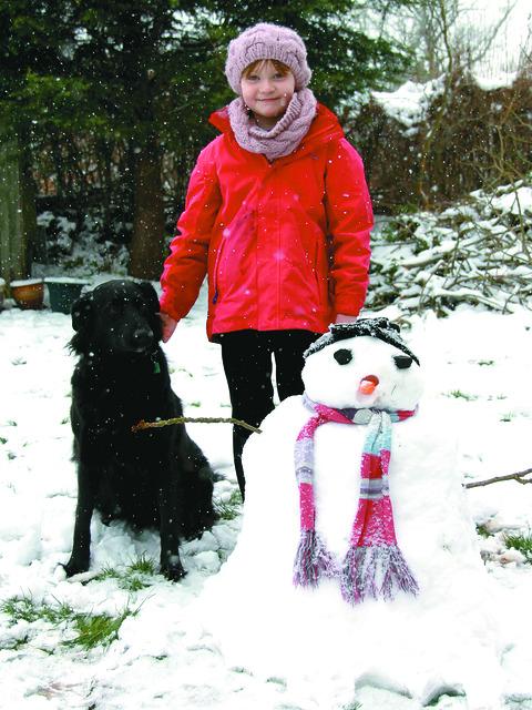 Mabel May braves a snow shower in her garden with her snowman and Annie the dog.